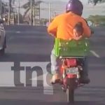 Momento en que un motorizado lleva a una niña en una cajilla, a bordo de una moto, en Managua
