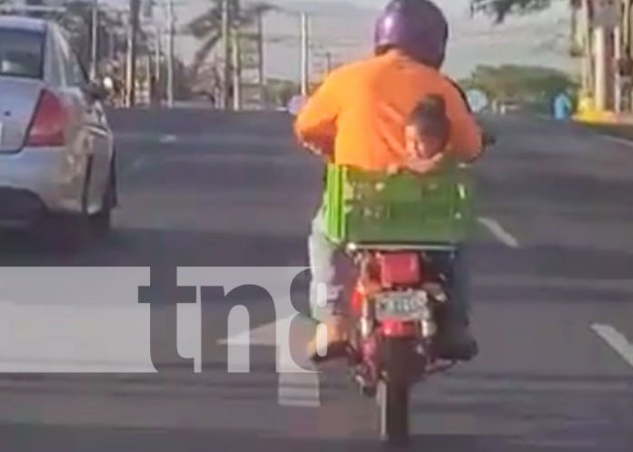 Momento en que un motorizado lleva a una niña en una cajilla, a bordo de una moto, en Managua