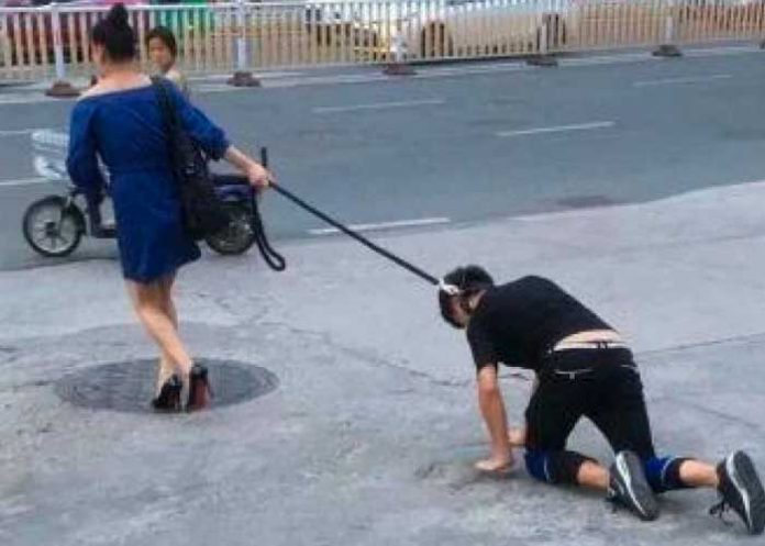 Mujer paseando a un hombre como si fuera un perro
